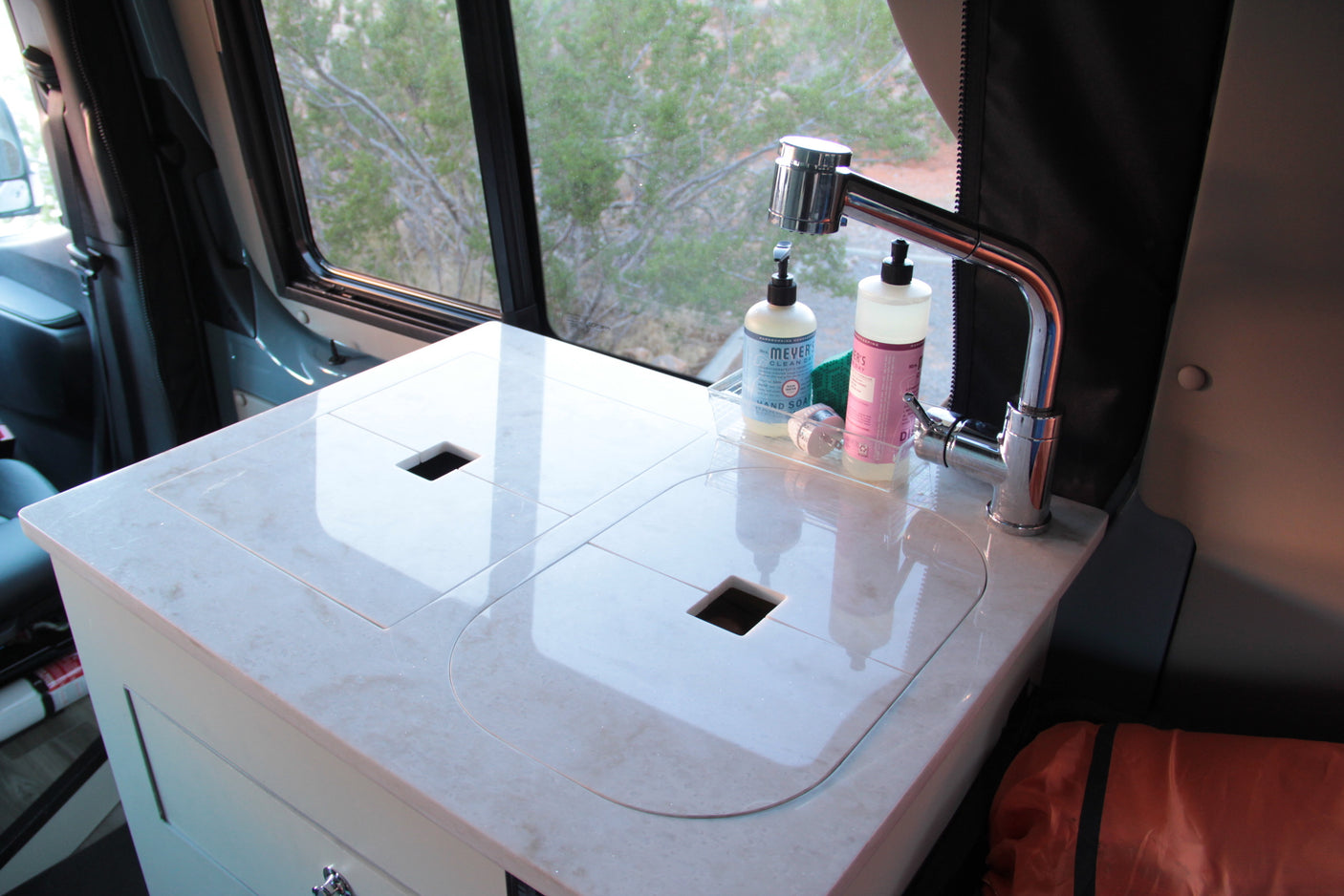 RV rental compact kitchen featuring a sink, faucet, and soap, with a view of nature outside the window.