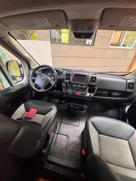 Ram ProMaster rv rental van interior: cockpit view with dashboard, steering wheel, and front seats holding keys.