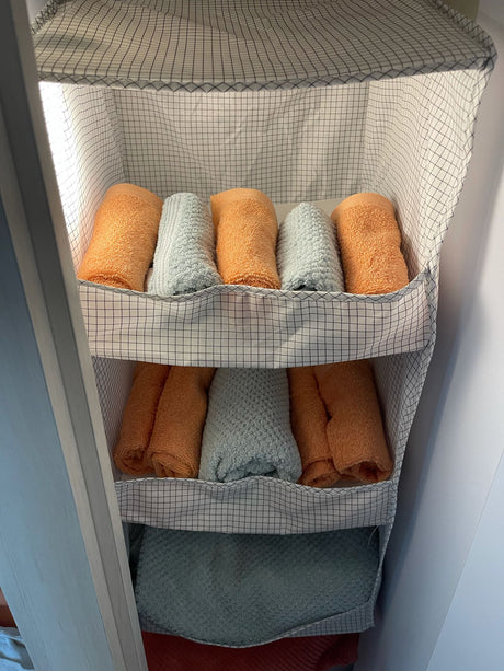 Hanging fabric organizer with neatly rolled orange & light blue towels, ideal for RV rental storage. Maximizing space inside a compact area.