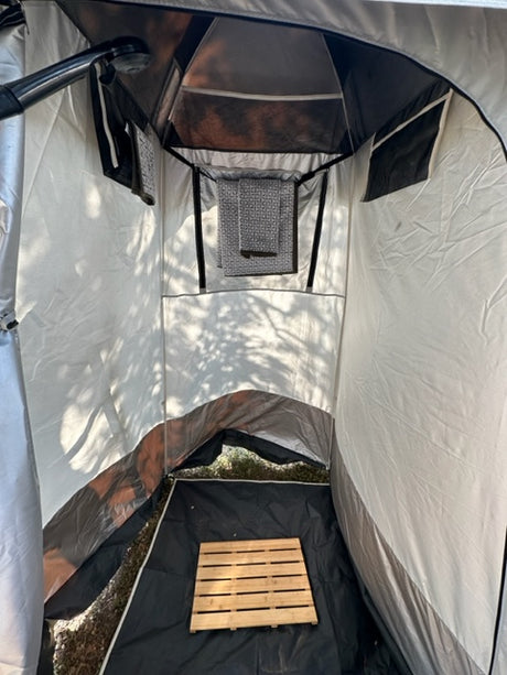 RV rental: Inside a well-equipped portable outdoor shower tent with a wooden mat & storage pockets.