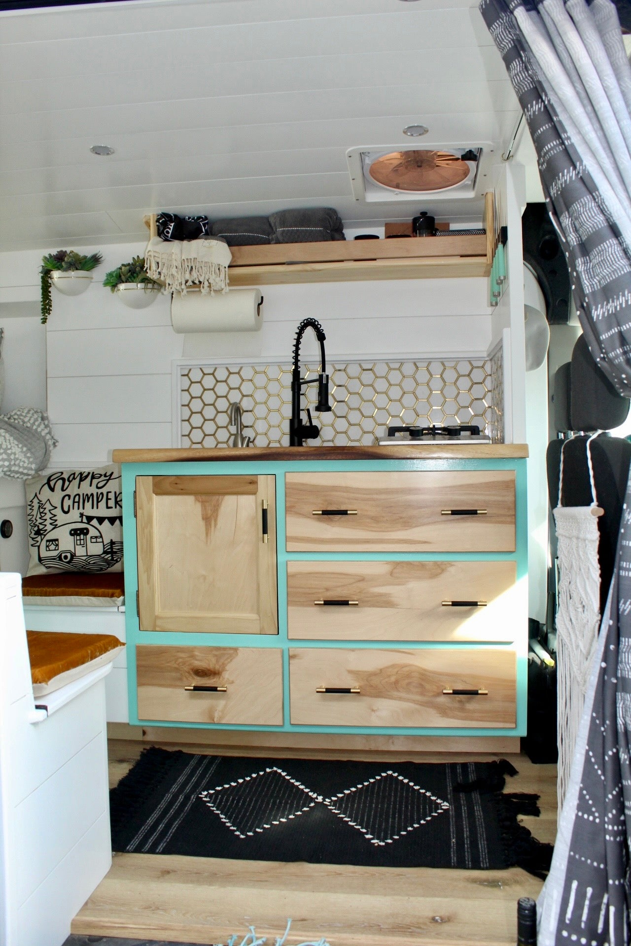 This RV rental offers a stylish kitchenette with a black faucet, honeycomb tiles, teal cabinets, and a patterned rug.