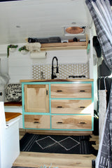 This RV rental offers a stylish kitchenette with a black faucet, honeycomb tiles, teal cabinets, and a patterned rug.