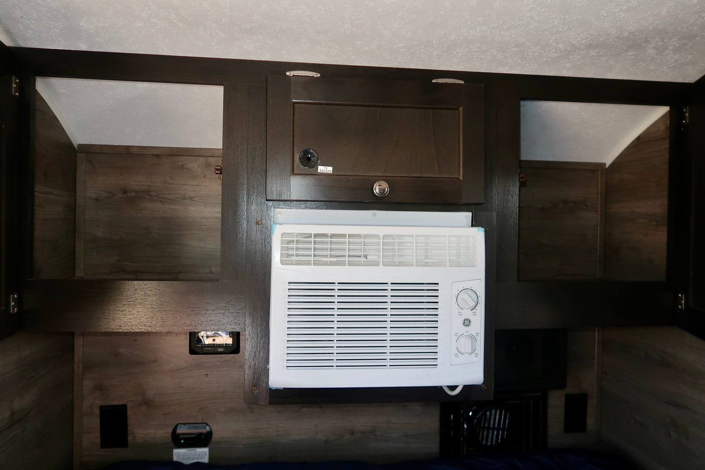 Inside an RV rental, featuring dark wood cabinets, a white GE air conditioner, and wood walls for a comfortable, practical space.