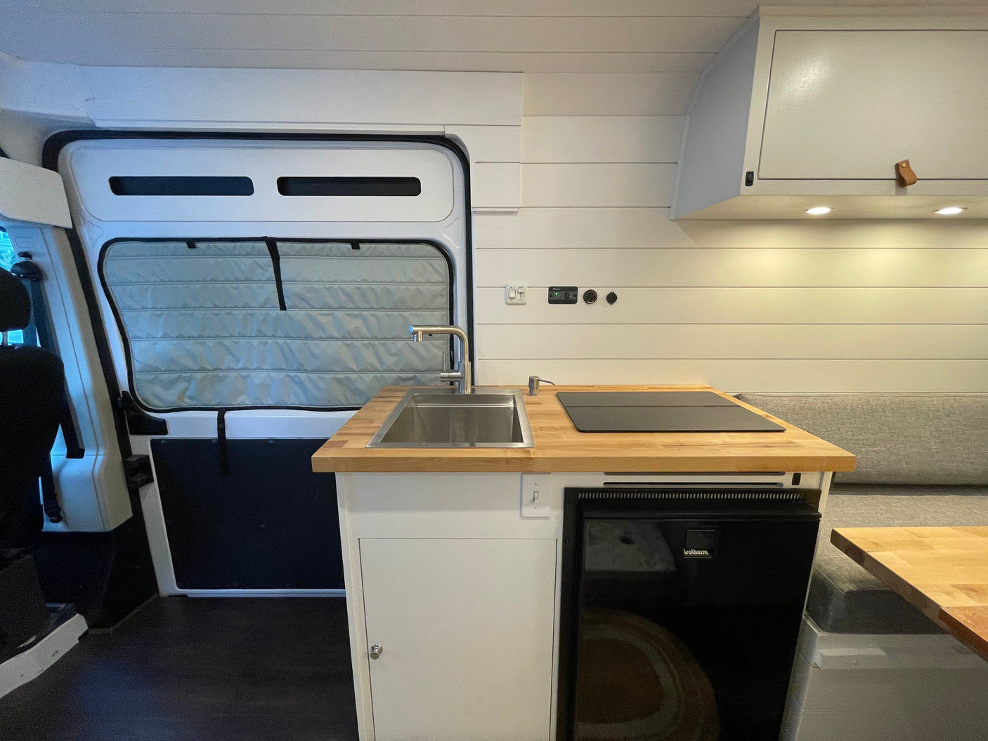 This RV rental boasts a compact camper van kitchen with sink, induction cooktop, fridge, and stylish wood counters.