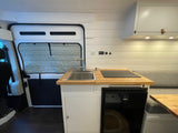 This RV rental boasts a compact camper van kitchen with sink, induction cooktop, fridge, and stylish wood counters.