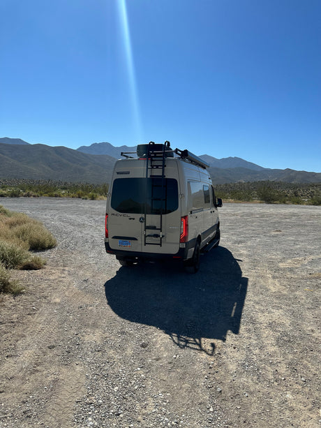 Winnebago Revel rv rental van on a desert road, mountains in background, under a bright blue sky. Perfect for adventure.