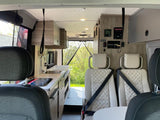 RV rental interior: kitchenette, two passenger seats, control panel, and rear exit to nature.