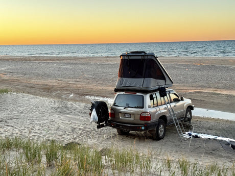James Baroud Discovery Xtreme XXL rooftop tent fully deployed on a Toyota Land Cruiser parked on a Lake Michigan beach at sunset, ladder down
