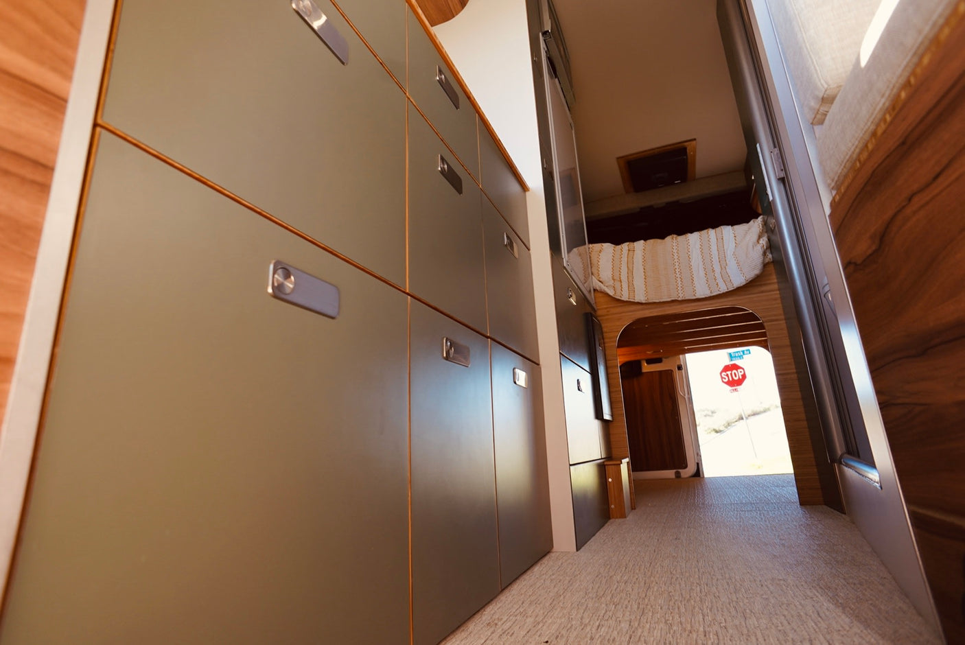 Spacious RV rental interior featuring modern storage, a cozy bed, and an open rear revealing an outdoor stop sign.