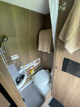 RV rental's compact wet bath featuring toilet, sink with integrated shower, curtain, and wood-look walls.