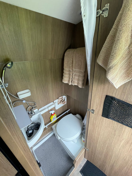 RV rental's compact wet bath featuring toilet, sink with integrated shower, curtain, and wood-look walls.