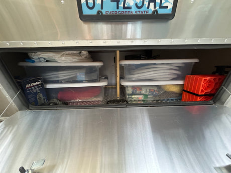Organized RV rental exterior storage: hoses, an ACDelco jack, and orange leveling blocks in clear bins.