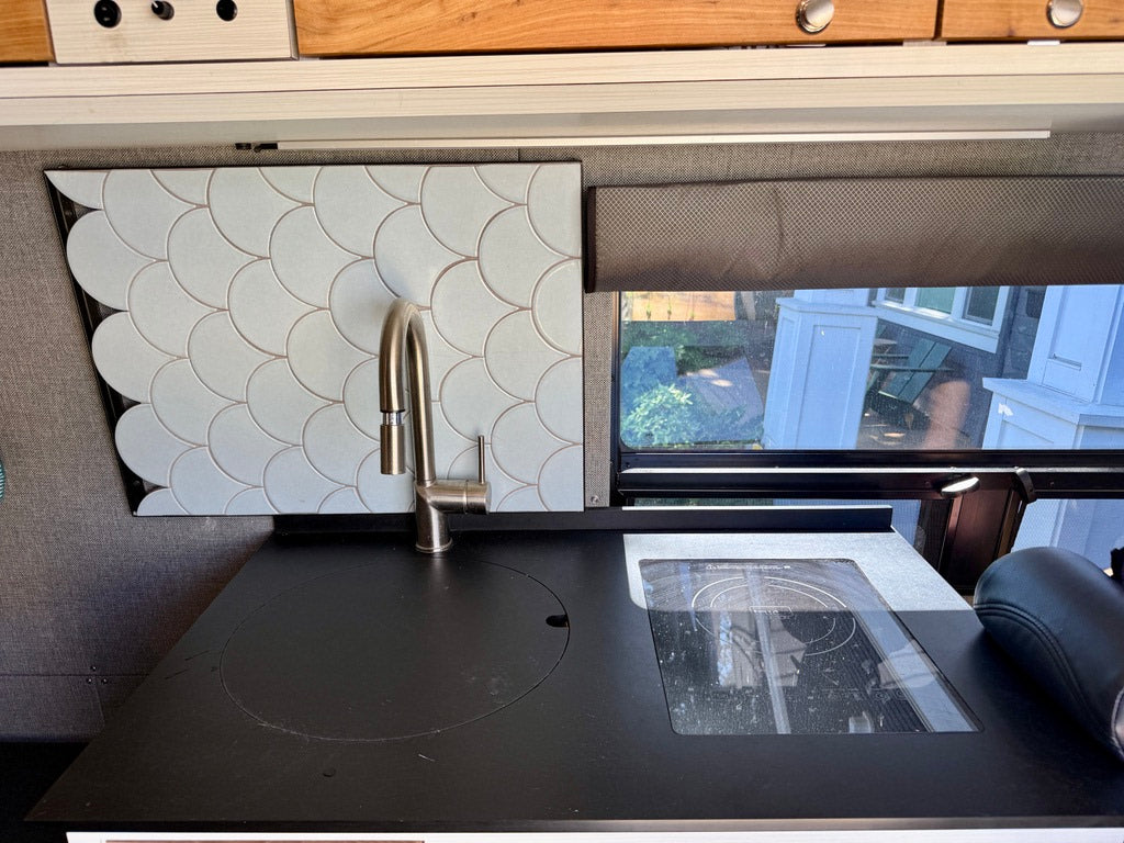 Modern RV rental kitchen: sleek black counter with a modern sink, induction cooktop, and stylish light blue scallop tile backsplash.