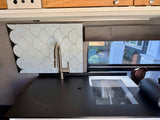 Modern RV rental kitchen: sleek black counter with a modern sink, induction cooktop, and stylish light blue scallop tile backsplash.