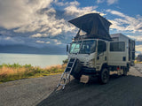 2021 Isuzu NPR Crew Cab 4x4 expedition rig with rooftop tent deployed, parked lakeside