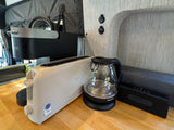RV rental kitchen setup: Keurig, Bella toaster, and Elite Gourmet kettle on a wood counter, plus a soundbar. Perfect for glamping.