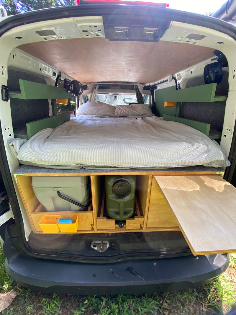 View from the rear of an rv rental camper van. Features a comfortable bed, overhead shelves, and under-bed storage for toilet & water. — photo 8