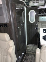 Modern RV rental interior: cream captain's chair, dark wood panels, galley, and compact bathroom door with frosted oval window.