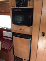 Inside this **rv rental**, find a compact kitchen featuring a microwave, refrigerator, and a cozy red & white dinette.