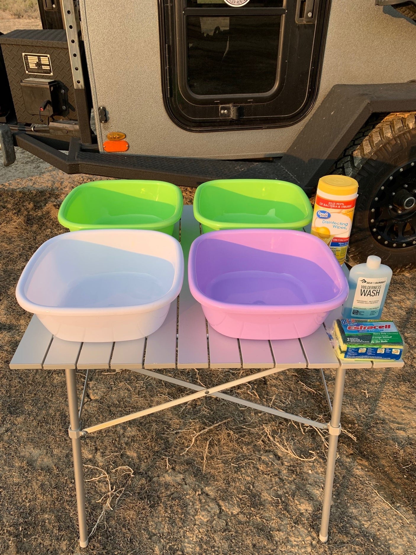 Portable wash station for RV rental camping, with colorful basins, wipes, and soap on a table outdoors.