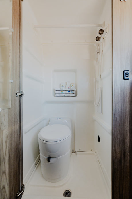 Bright white RV rental wet bath with toilet, shower, and caddy of toiletries.