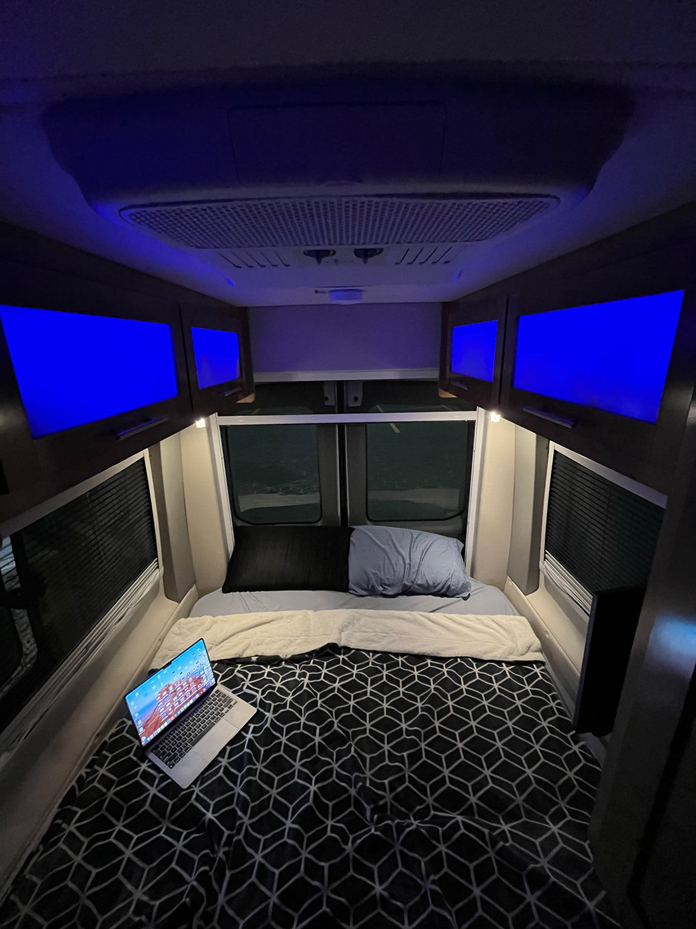 Inside an RV rental: a cozy bedroom setup with a laptop, bright blue screens, and patterned bedding.