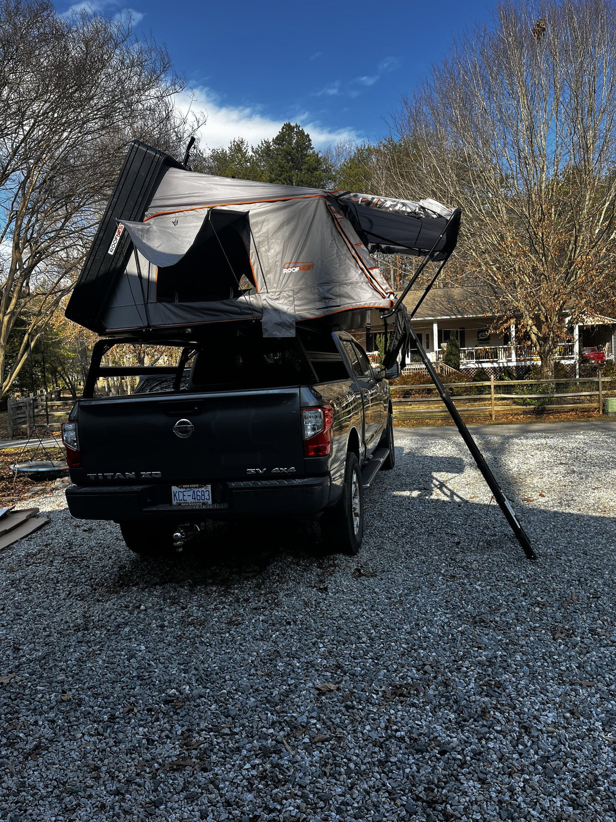 Rear three-quarter view of the Condor Overland 2XL deployed on the Titan XD bed rack with the Awnex awning arm extended to its ground pole, showing the hard top shell raised and the tent's orange-trimmed grey canopy — photo 2
