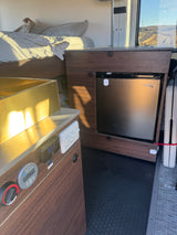 This rv rental features a well-equipped camper van interior: kitchen sink, RecPro fridge, bed, and Victron power systems.