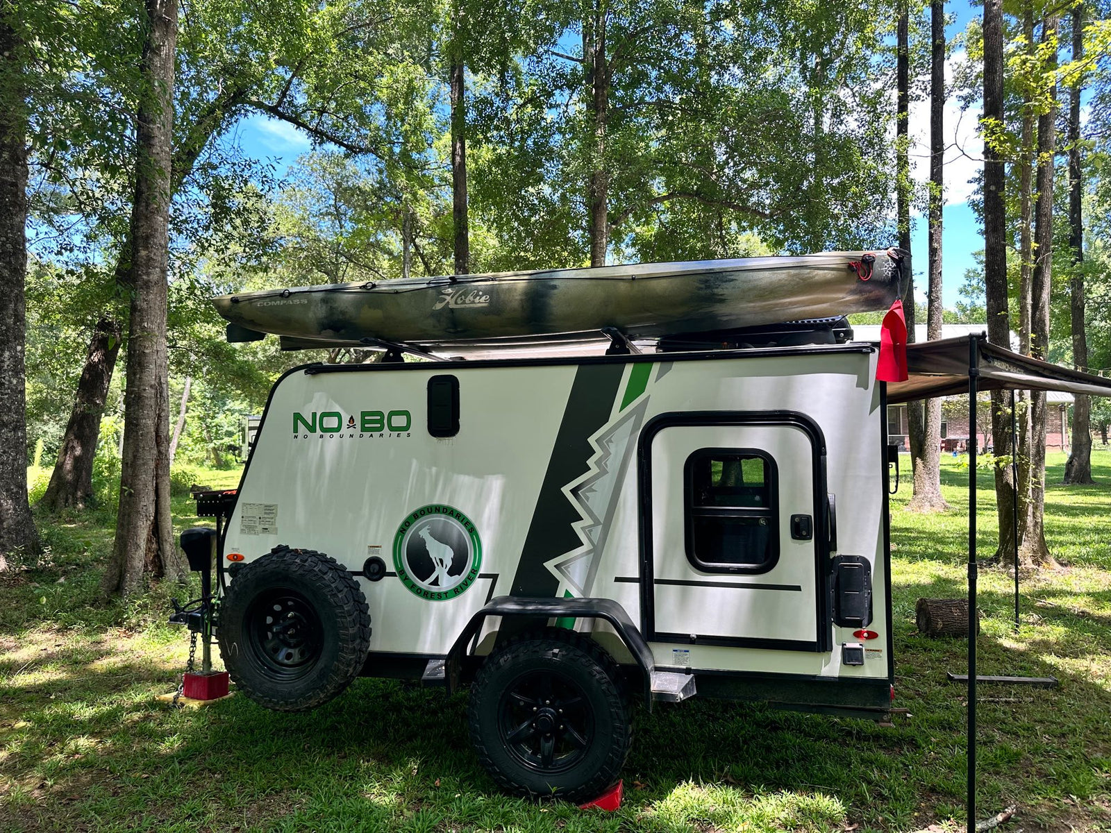 Compact rv rental with a Hobie kayak on top, set up in a shaded natural campsite.