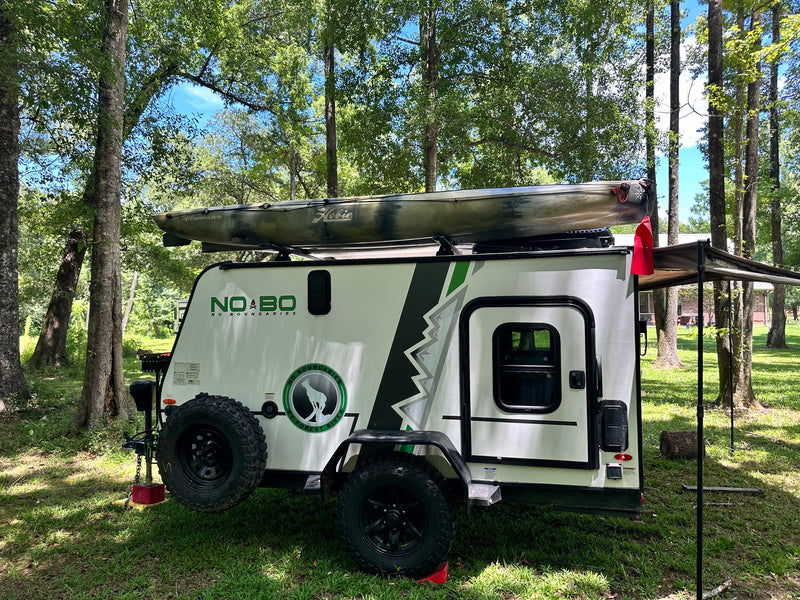 Compact rv rental with a Hobie kayak on top, set up in a shaded natural campsite. — photo 16