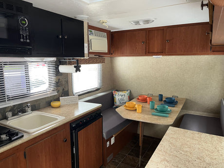 RV rental interior: A compact kitchen with sink & microwave on left, facing a colorful dinette on right. Ideal for travel.