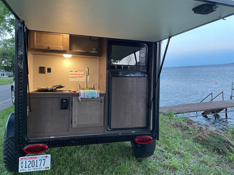 RV rental's outdoor kitchen (microwave, sink, fridge) by a lake. Perfect for scenic road trip camping.