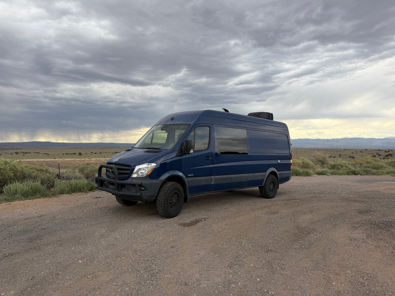 Dark blue Sprinter van RV rental parked on a gravel road, with a cloudy sky overhead and vast, open landscape behind it. — photo 2