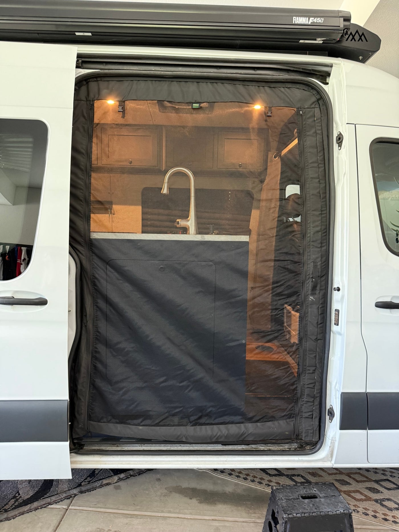 RV rental: view inside through mosquito screen door showing kitchen sink & lights. Fiamma awning above van door. — photo 17