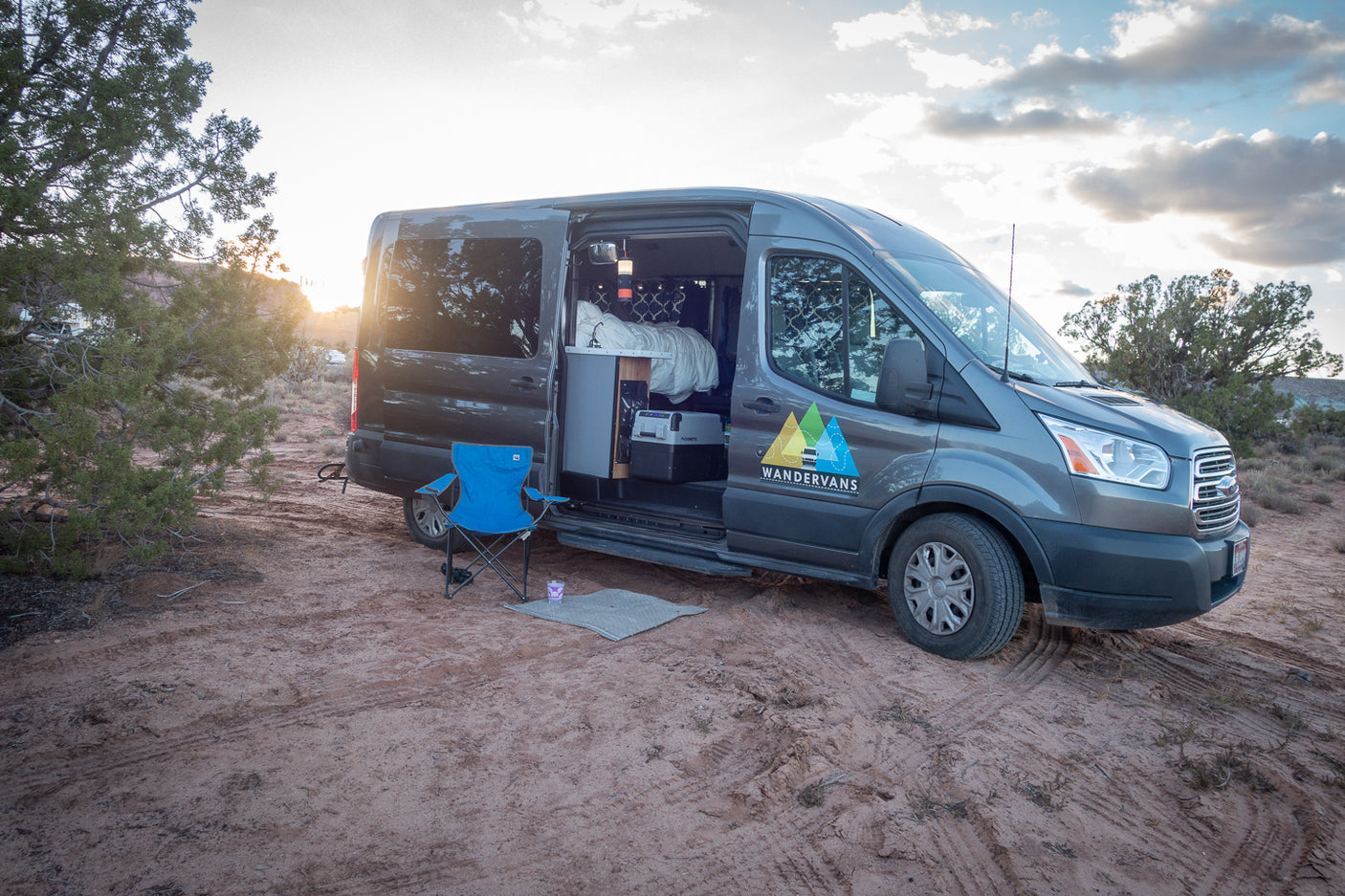 This grey camper van RV rental is parked at sunset, ready for your next adventure. The side door is open, showing the cozy interior.