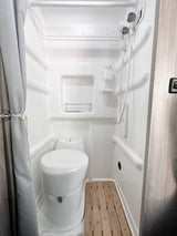 RV rental: Bright, compact bathroom with white toilet, handheld shower, and a wooden slat floor mat for a comfortable stay.