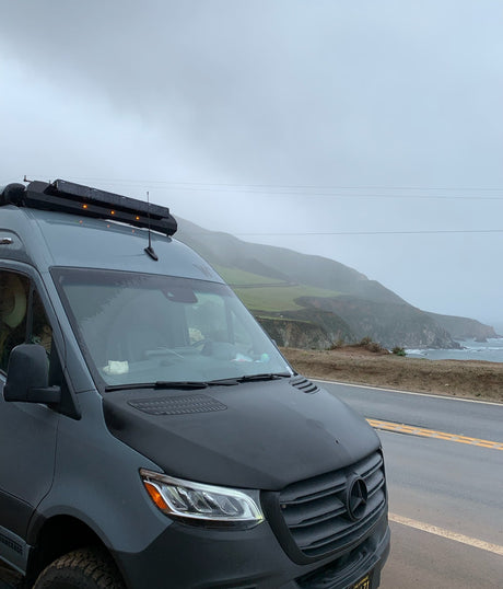 RV rental: A customized Mercedes Sprinter van parked on a scenic, misty coastal highway.