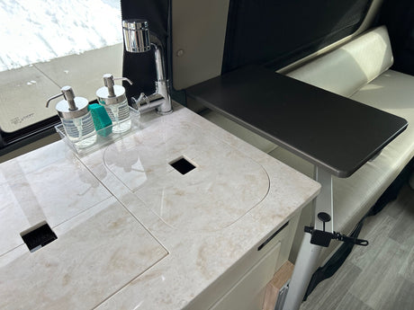 Inside an RV rental: a modern kitchen with a light-colored counter, sink, faucet, and a dark table by a cream bench.