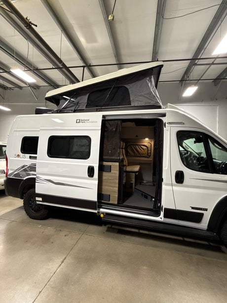 White Winnebago Solis camper van with open pop-top tent and interior, parked indoors. Ideal for your next RV rental trip.