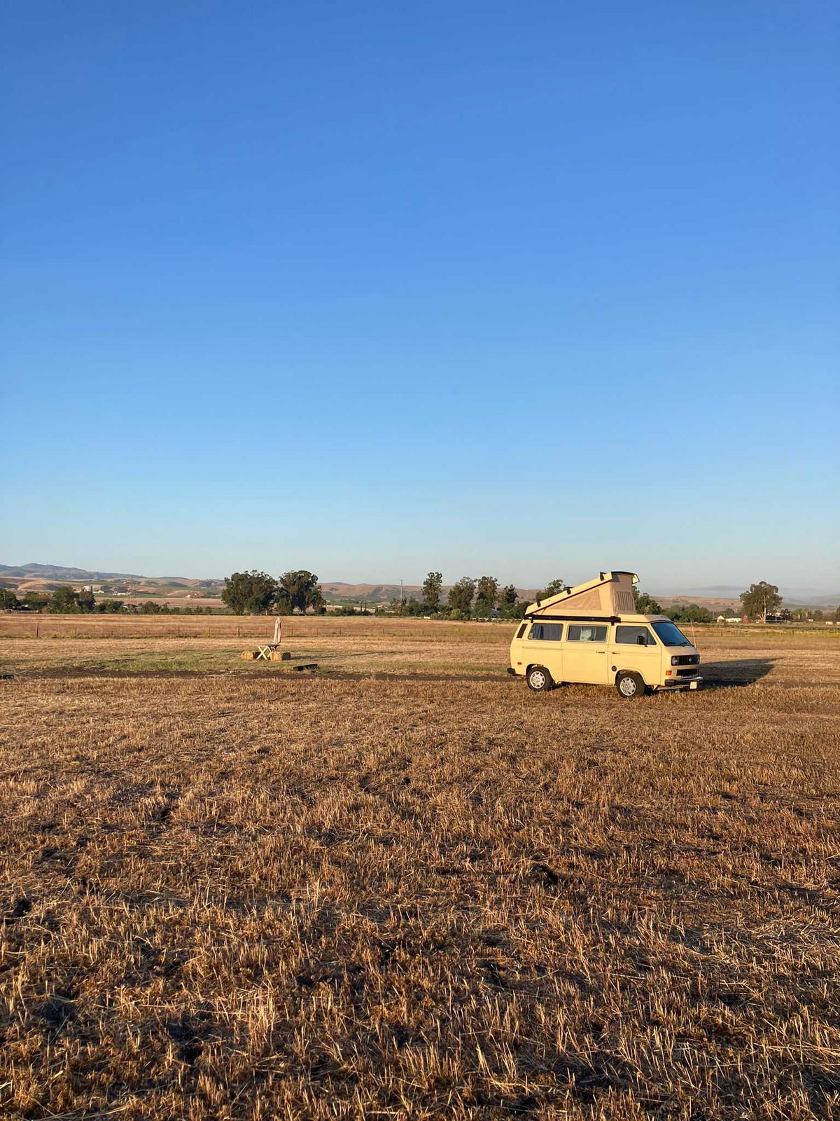 parked beside a tranquil mountain lake and forest pines.|Tan pop-top camper van parked at a forest campsite with an awning extended — photo 10