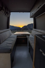 RV rental interior: cozy seating with a dining table overlooking a breathtaking mountain sunset. Perfect for van life adventures.