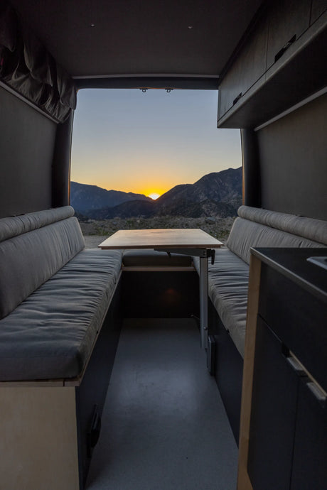RV rental interior: cozy seating with a dining table overlooking a breathtaking mountain sunset. Perfect for van life adventures.