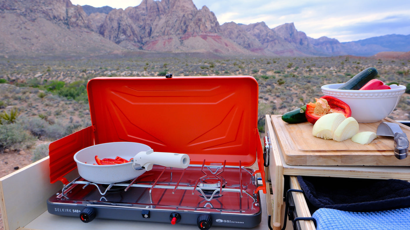 An rv rental makes outdoor cooking easy! A camping stove with fresh peppers & onions, set against a desert mountain view.