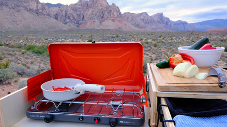 An rv rental makes outdoor cooking easy! A camping stove with fresh peppers & onions, set against a desert mountain view.
