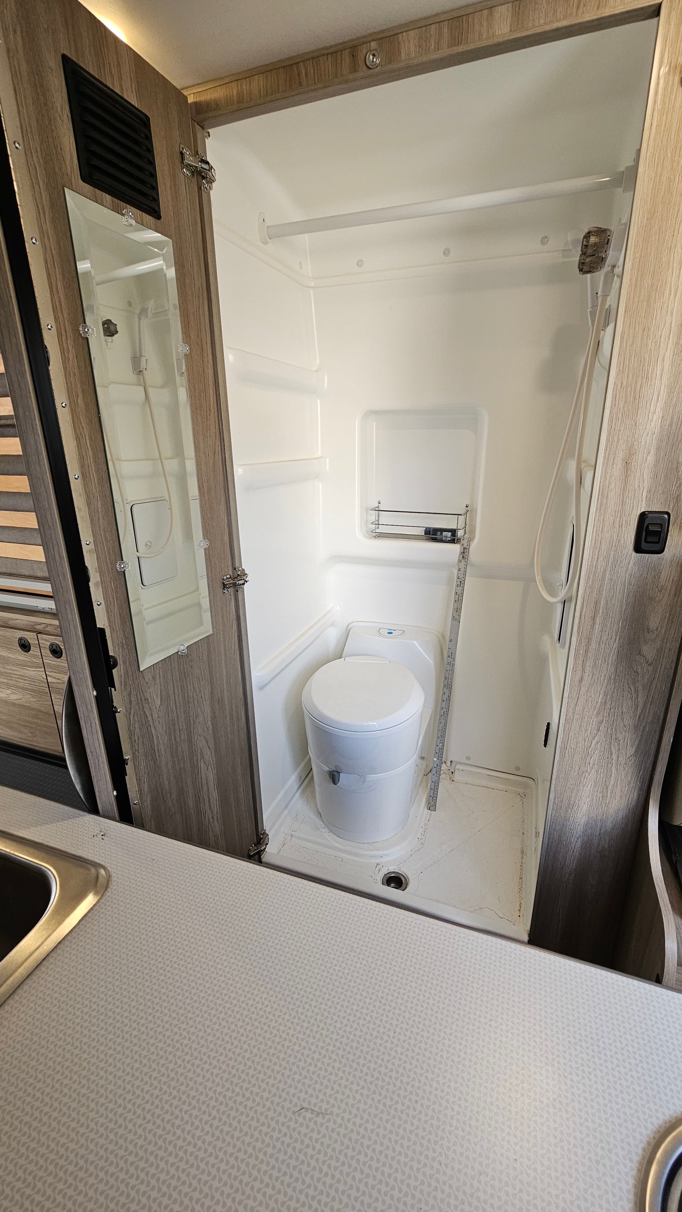 RV rental compact wet bath: white toilet, shower, and mirrored door inside the small cabin bathroom.