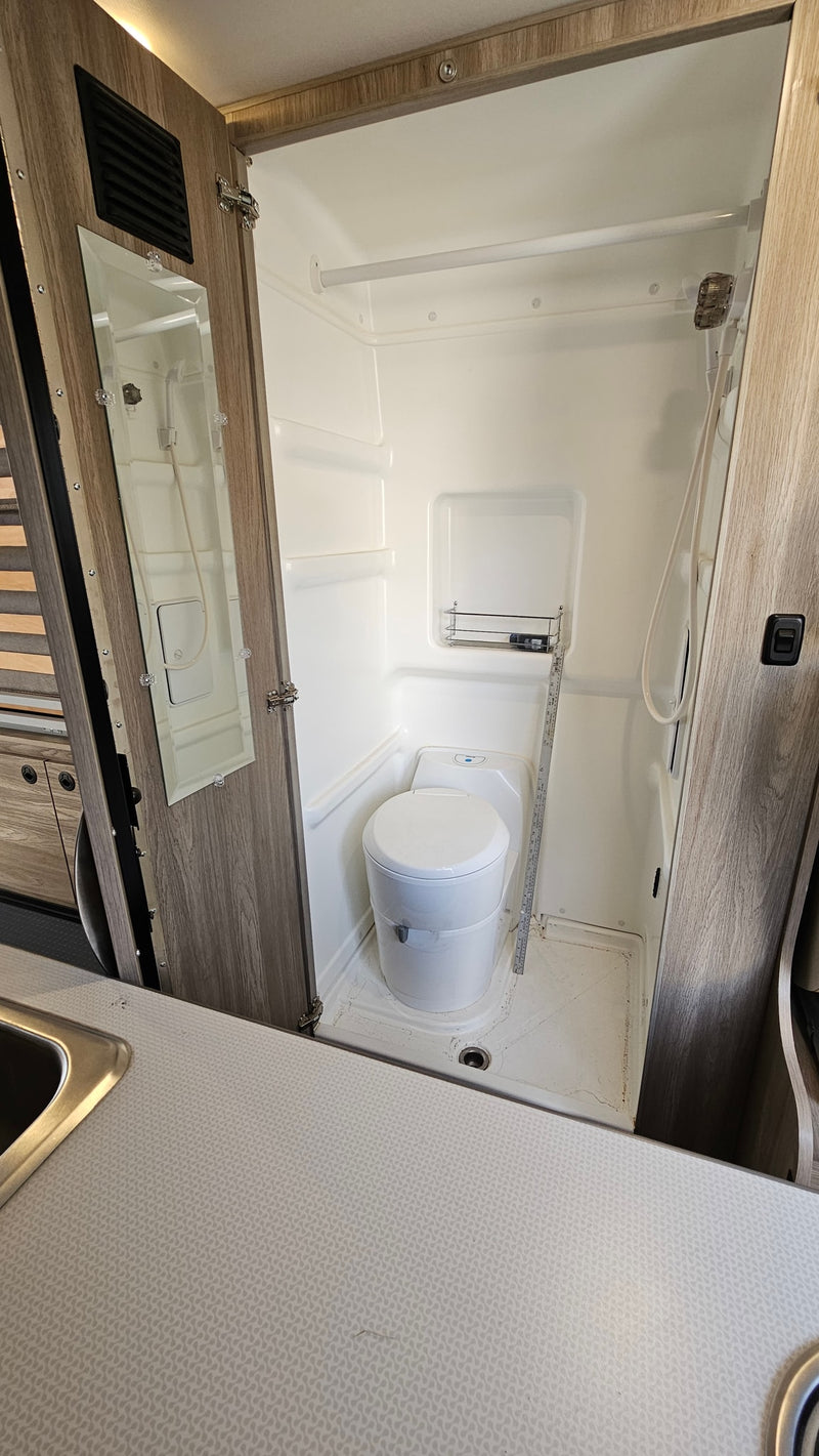 RV rental compact wet bath: white toilet, shower, and mirrored door inside the small cabin bathroom. — photo 4