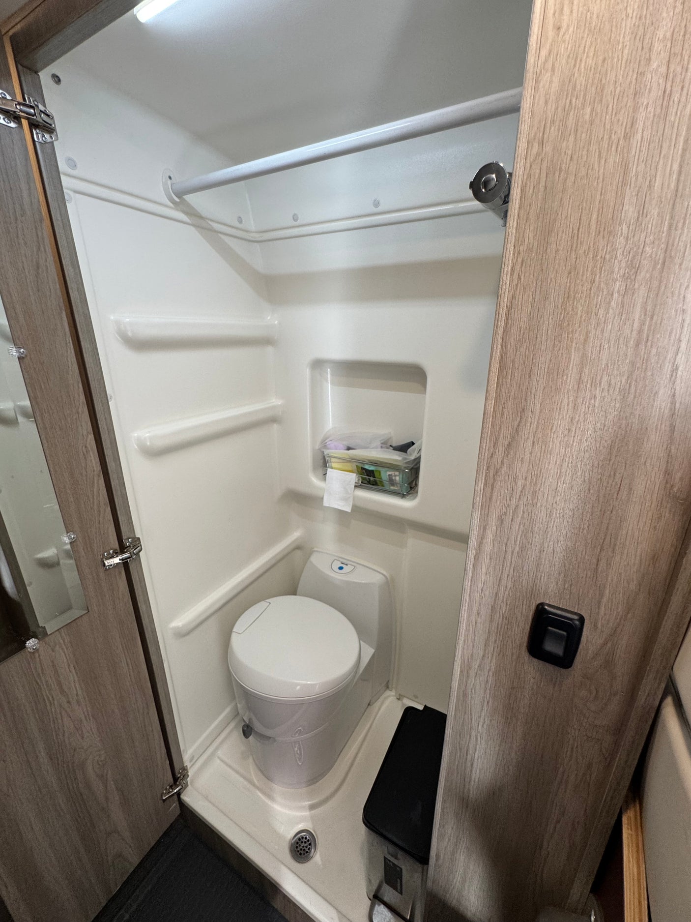 This compact RV rental bathroom includes an integrated shower, toilet, shower bar, and built-in shelves for essentials.