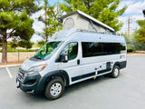 A sleek silver pop-top camper van, available for rv rental, is parked outdoors. Features a raised roof tent.