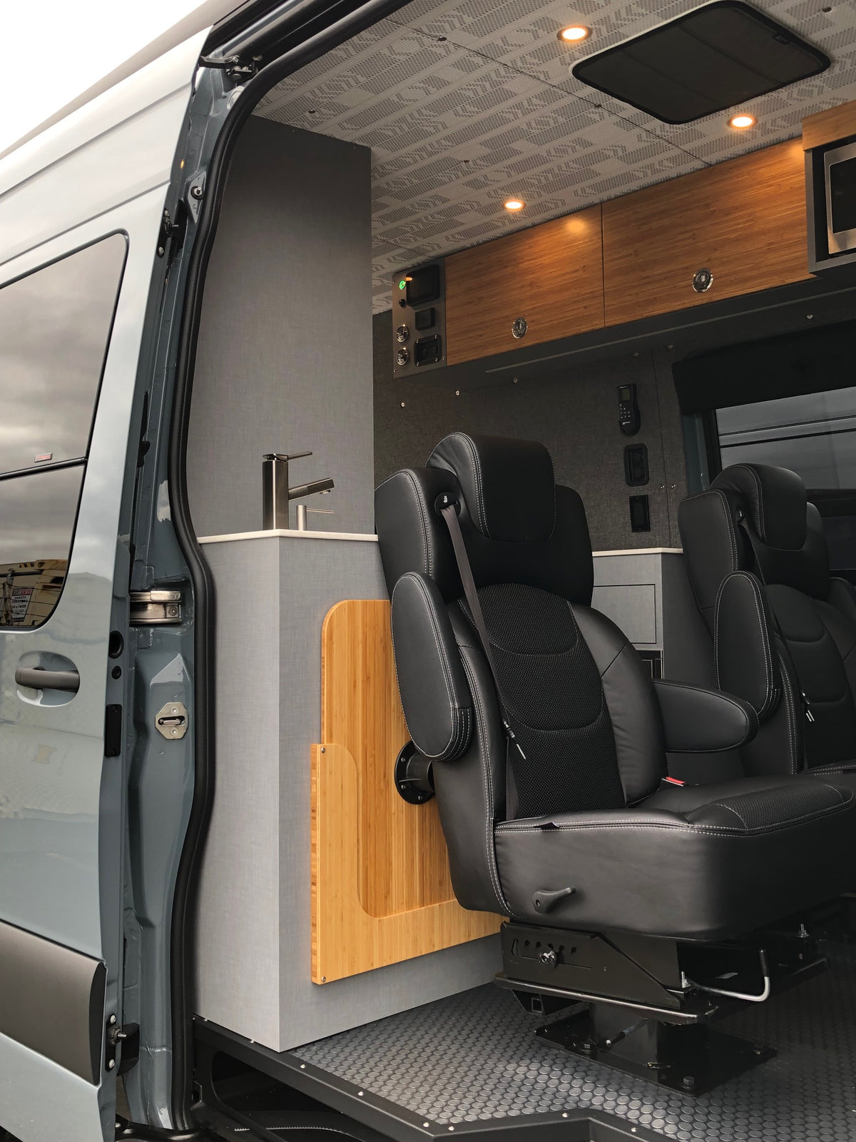 Luxury RV rental interior: spacious camper van with multiple black leather seats, wooden cabinetry, modern design. — photo 6