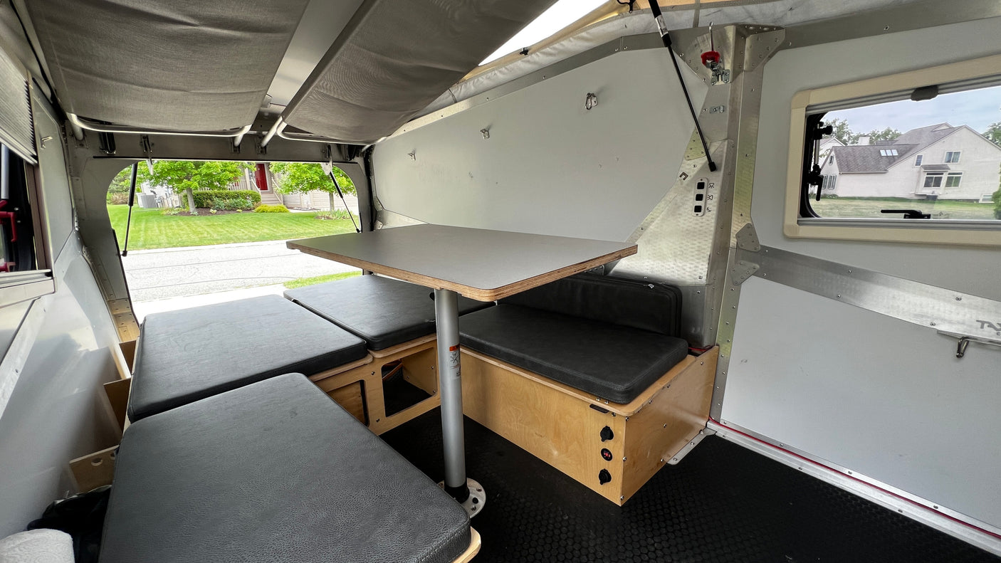 Inside a compact rv rental: a cozy dinette with dark cushions and a table, convertible to a sleeping area for comfortable travel.